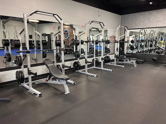Squat racks and adjustable benches along a mirrored wall
